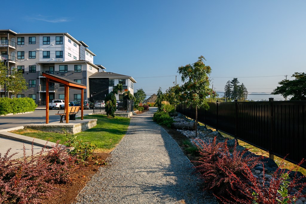 a path leading to a building with a black fence on the left and a building on the