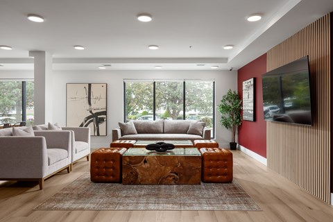 A modern living room with a grey sofa, a brown ottoman, and a flat screen TV mounted on the wall.