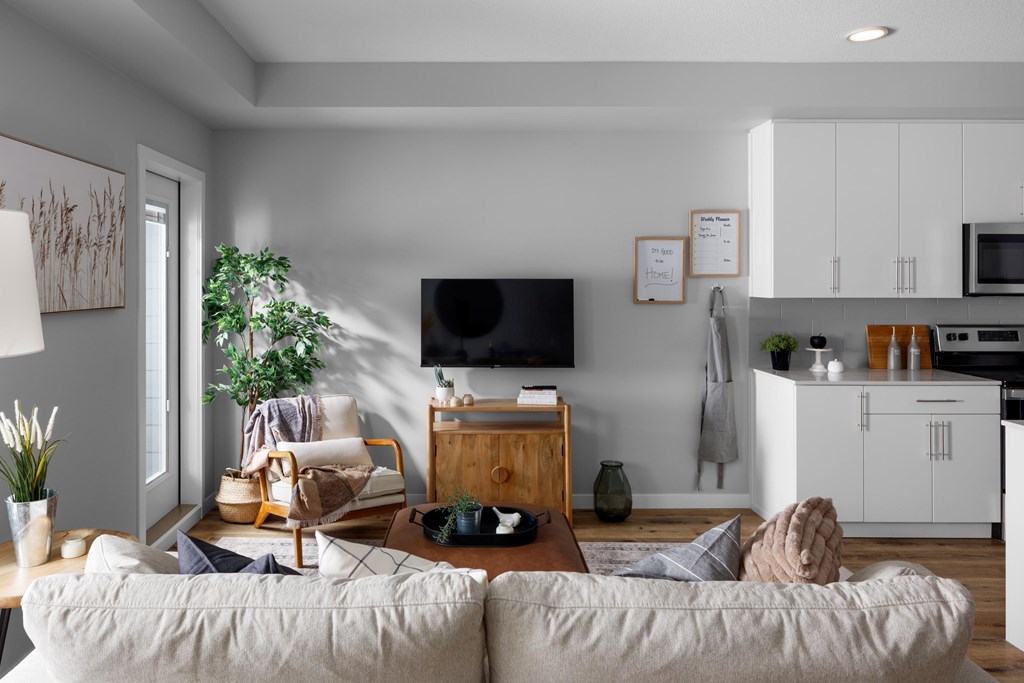 A modern living room with a large couch, a television, and a kitchen area in the background.