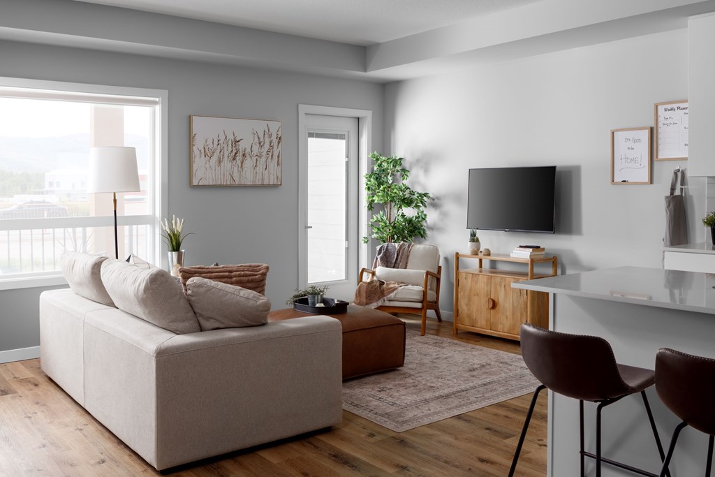 A living room with a white couch, a wooden coffee table, a flat screen TV, and a large window.