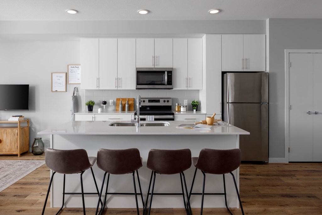 A modern kitchen with a white island and three chairs.