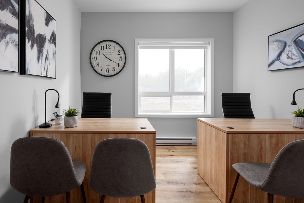 A room with two desks and chairs, a clock on the wall, and two paintings.