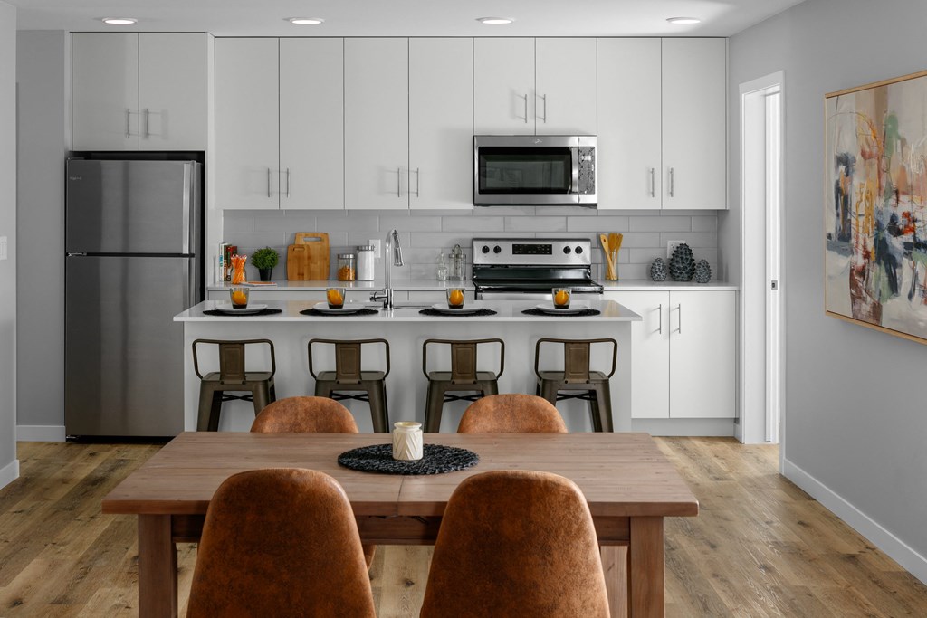 a kitchen with white cabinets and a large island with a wooden table and chairs