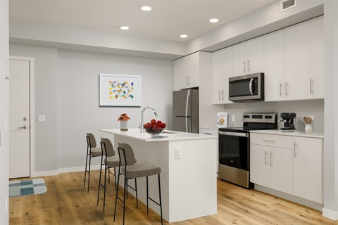A kitchen with white cabinets and a white island with chairs around it.