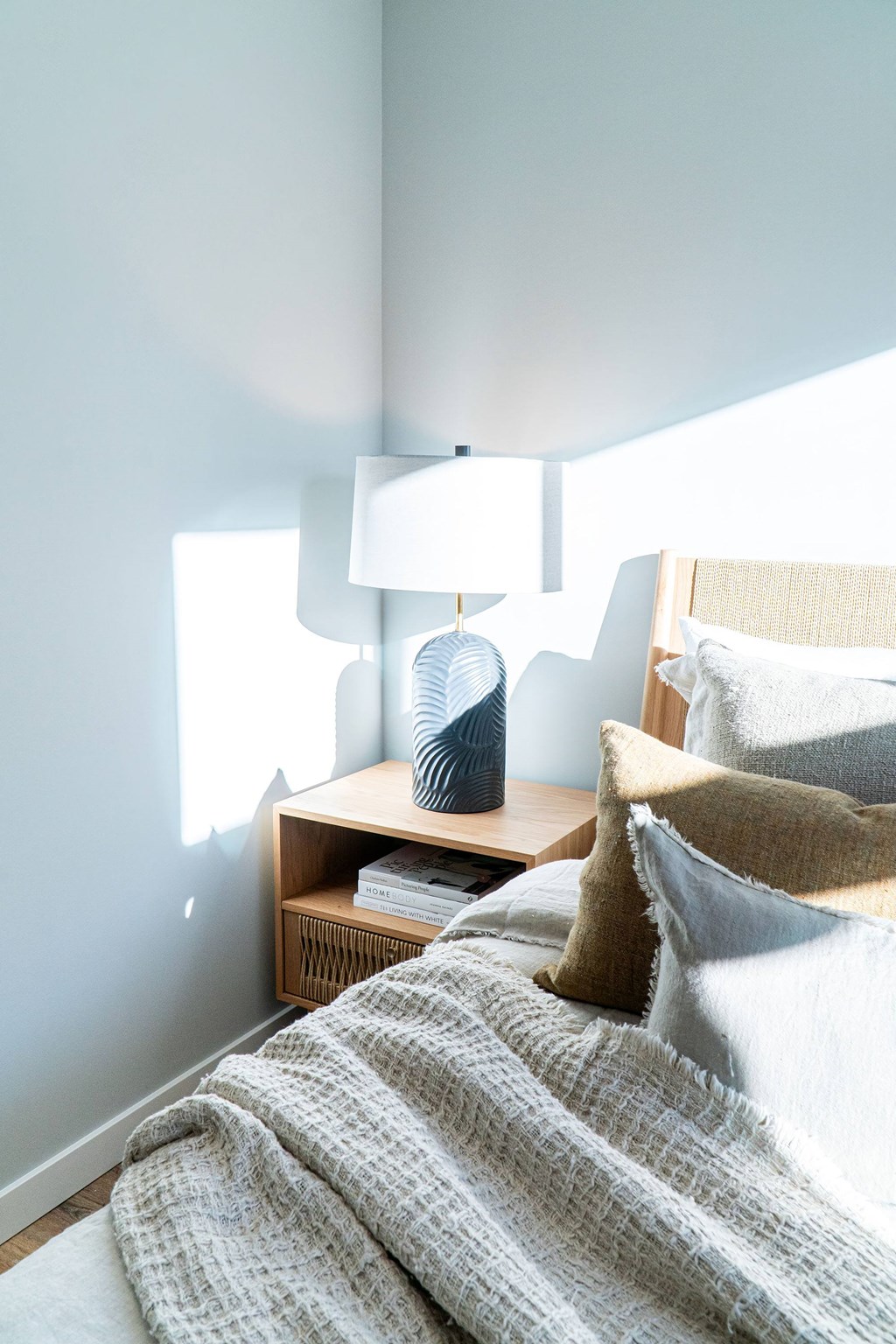 A bedroom with a bed, a nightstand with a lamp, and a basket on the nightstand.