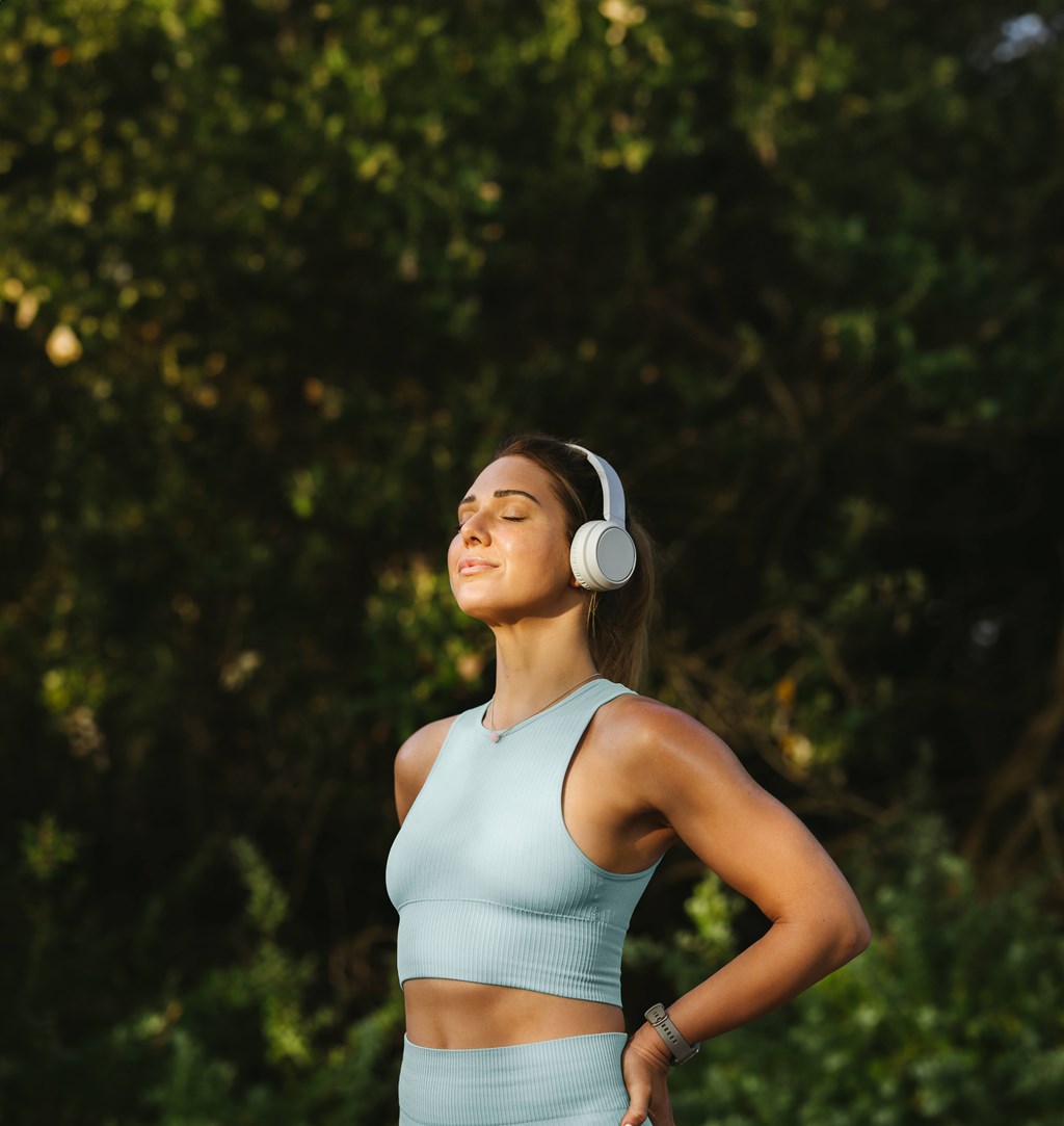 A woman in a blue top and skirt is listening to music with white headphones.