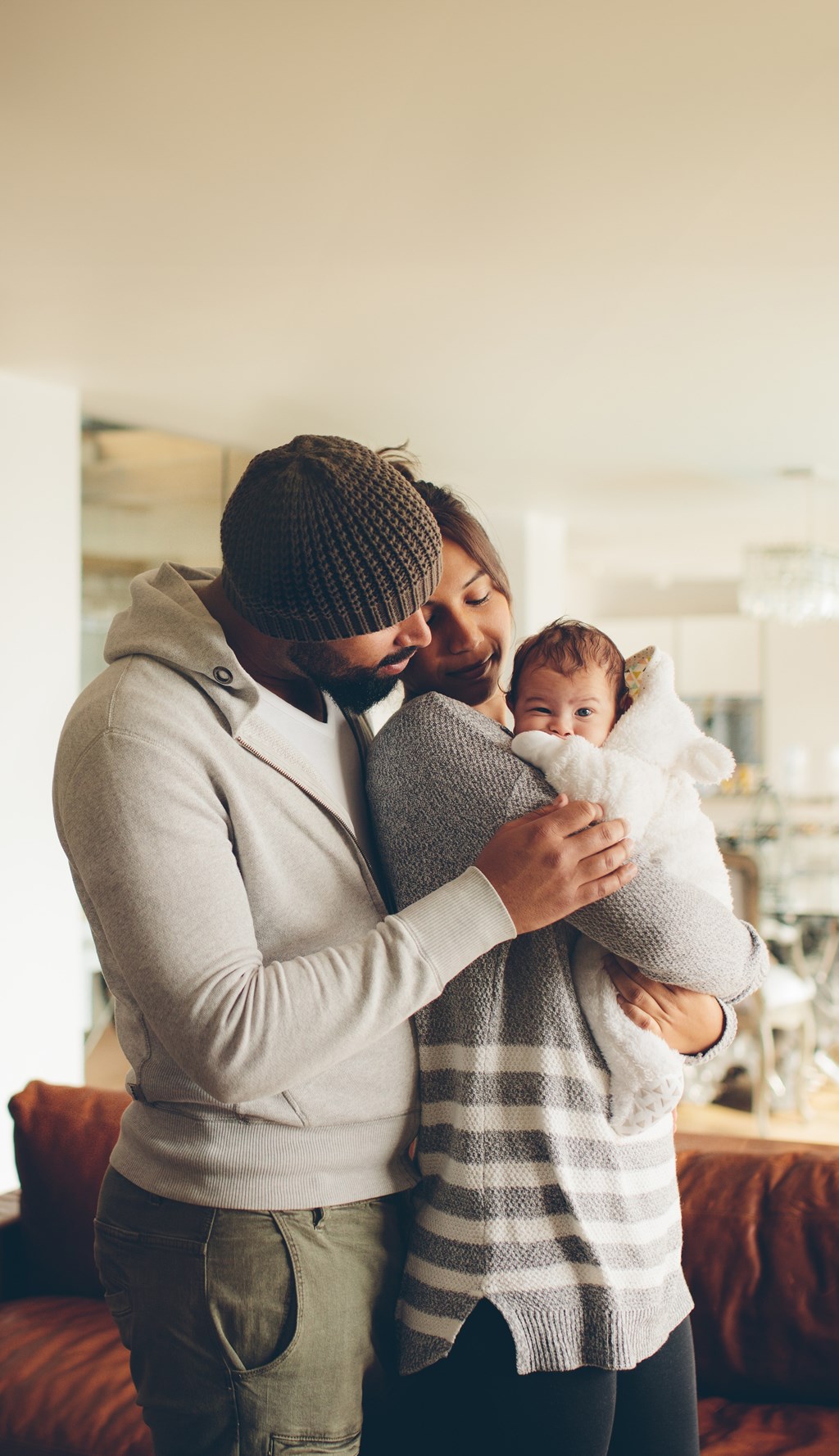A man in a beanie and a woman in a striped sweater are holding a baby.