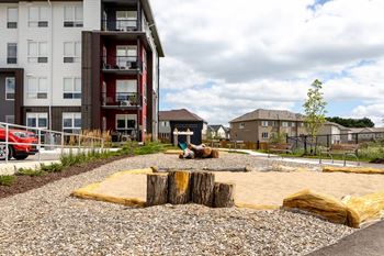 a playground with logs and rocks in front of an apartment building