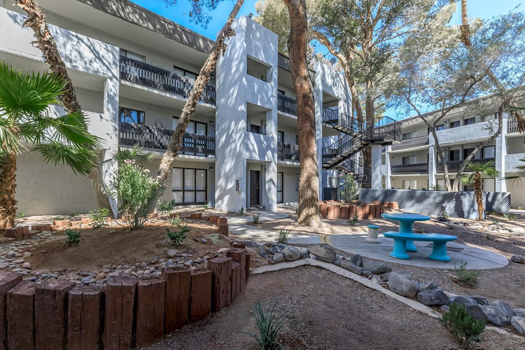 a courtyard with a blue bench and a building with trees at Evoq Apartment Homes, Las Vegas Nevada  