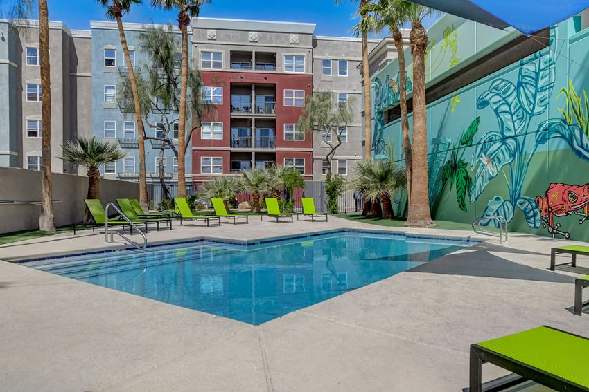 a swimming pool with green lounge chairs and a mural on the side of a building