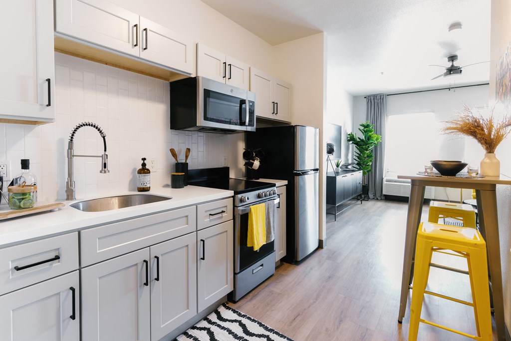 a kitchen with white cabinets and black appliances and a yellow bar stool