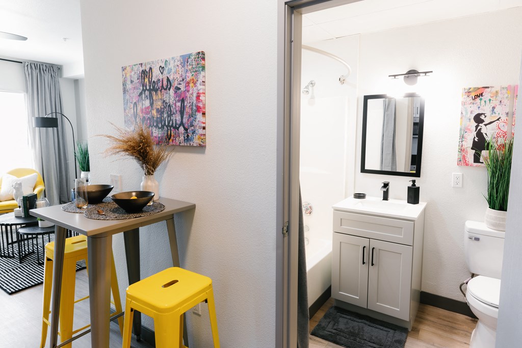a small kitchen and bathroom with yellow stools and a table
