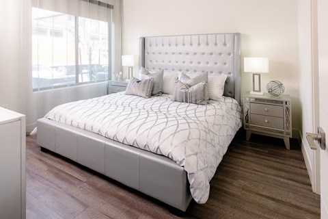 A bed with a white headboard and pillows is in a room with wooden flooring.