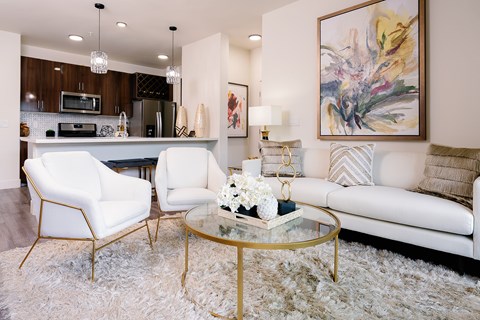 A modern living room with a white sofa, two white chairs, and a glass coffee table.