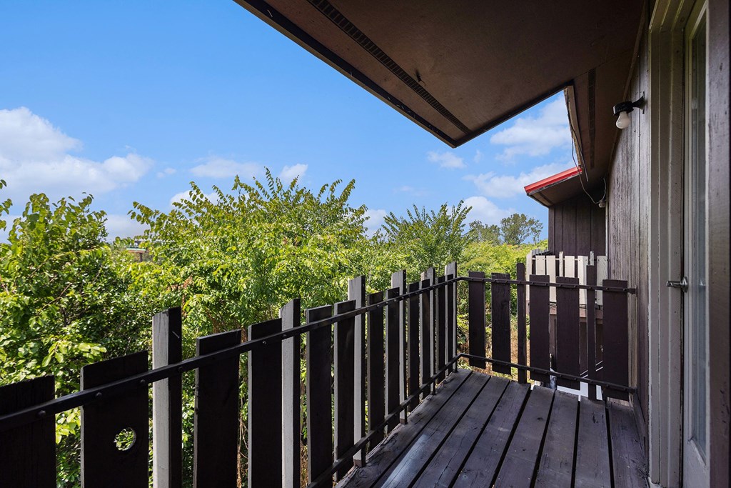a balcony with a wooden railing and trees in the background