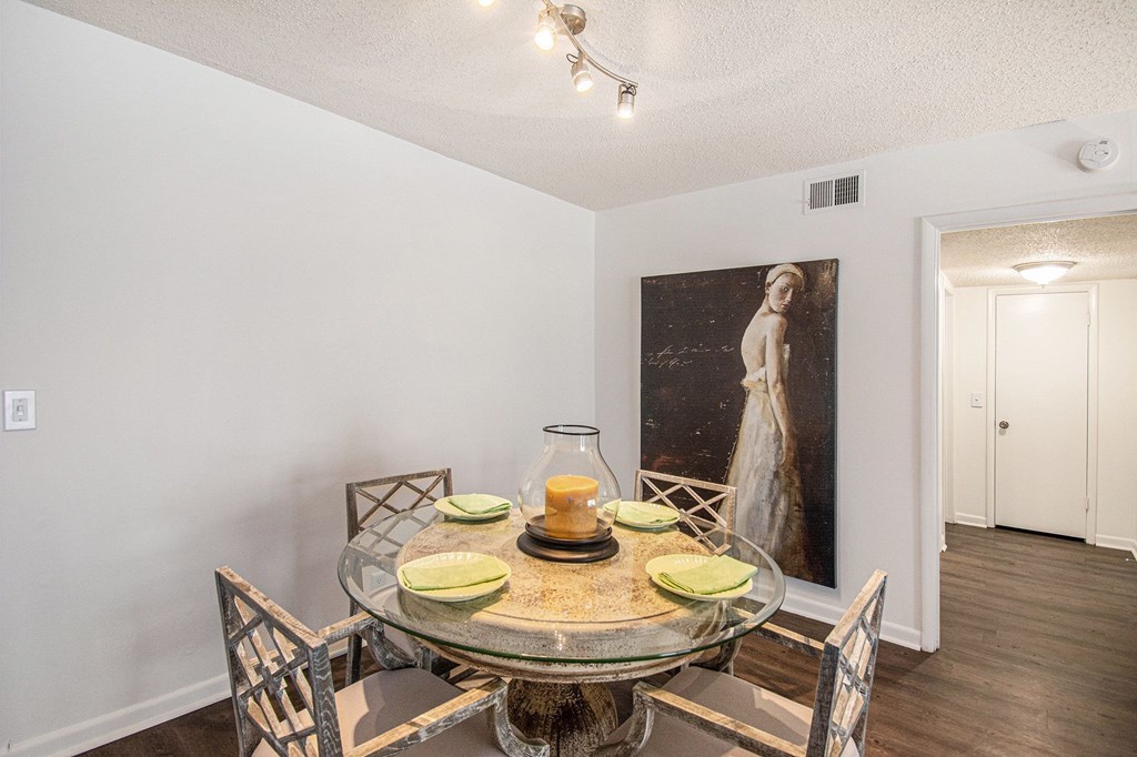 A dining room with a glass table and chairs and a painting on the wall.