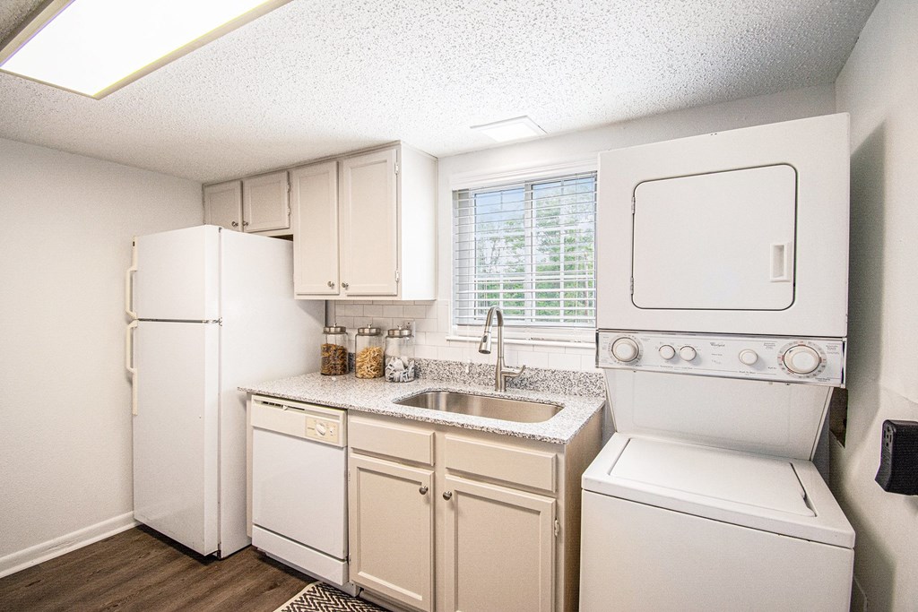 A small kitchen with white appliances and a window with blinds.
