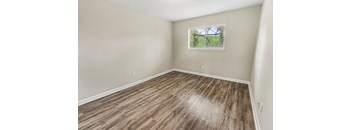 A room with wooden flooring and a window showing trees outside.
