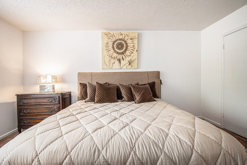 A bed with a quilted cover and a wooden nightstand with a lamp.
