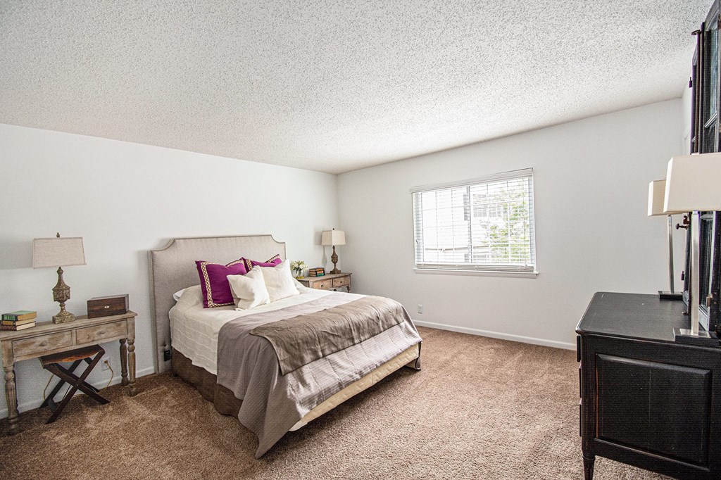 A bedroom with a bed, nightstand, and window.