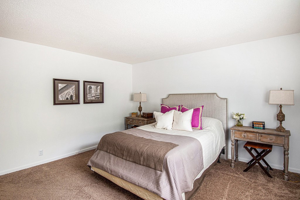 A bedroom with a bed, nightstand, and two framed pictures on the wall.
