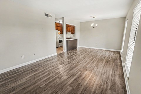 A room with wooden flooring and a kitchen in the background.