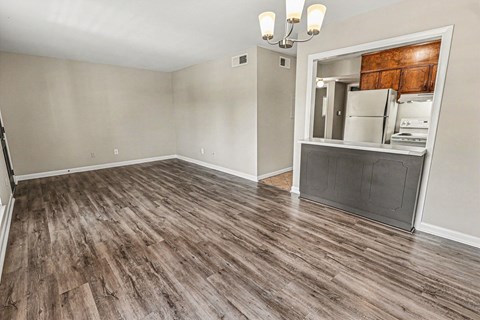 A room with wood flooring and a kitchenette in the background.