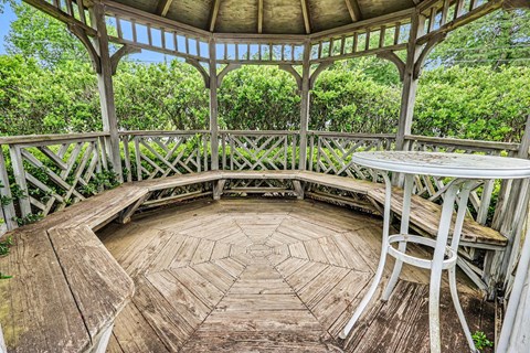 A wooden gazebo with a table and chairs in the middle of a circular deck.