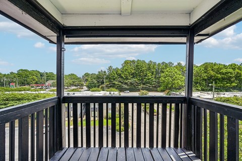 A wooden deck with a view of a parking lot and trees.