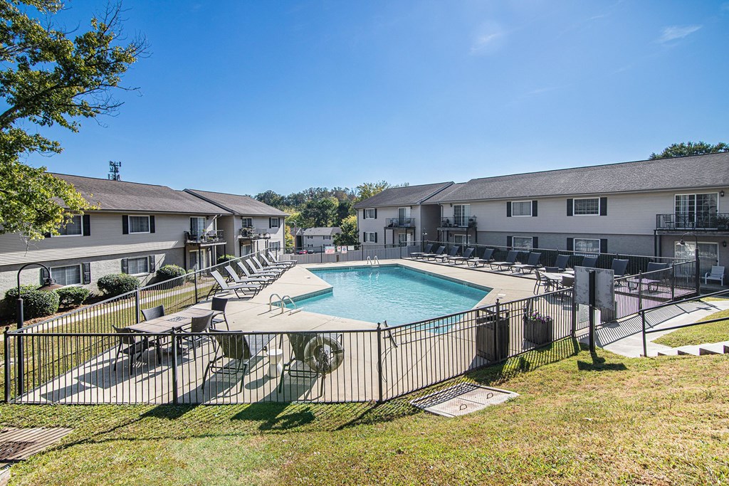 A swimming pool surrounded by a fence and chairs in a sunny day.