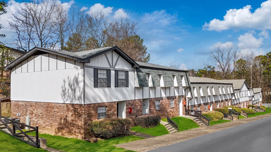 A white building with a grey roof is surrounded by greenery.
