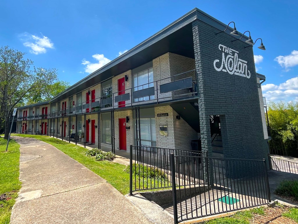 The Nolan Apartments building has a black fence and a green lawn in front.