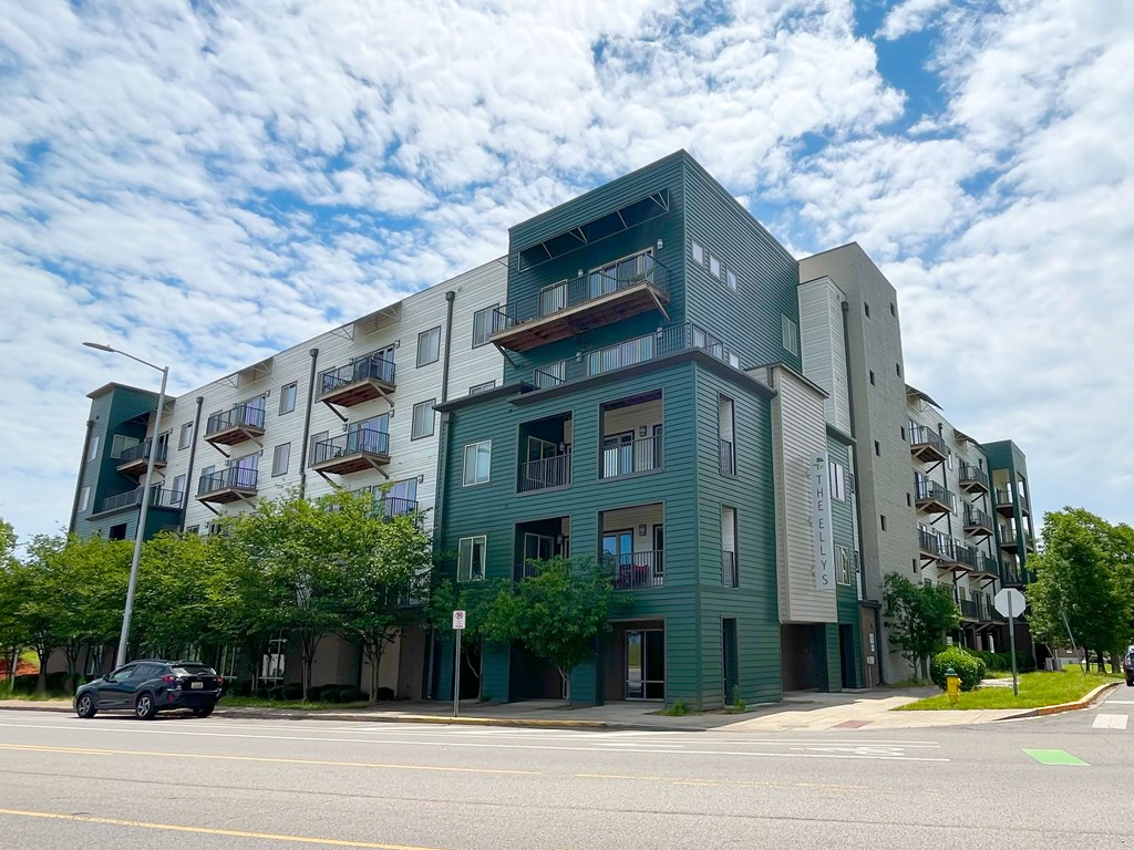 A modern apartment building with balconies and a car parked in front.