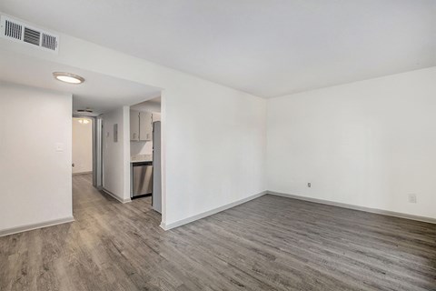 the living room of an apartment with white walls and wood flooring