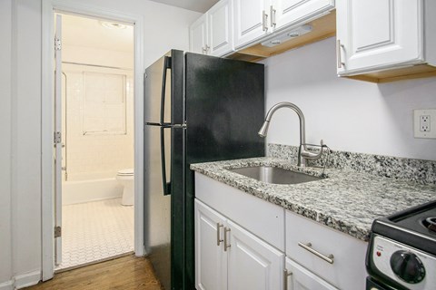 A black refrigerator in a kitchen with white cabinets.