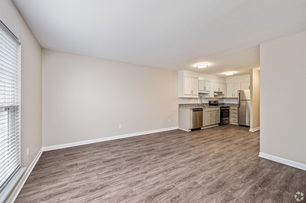 A kitchen area with a sink, stove, and refrigerator is visible through a window in a room with wooden flooring.