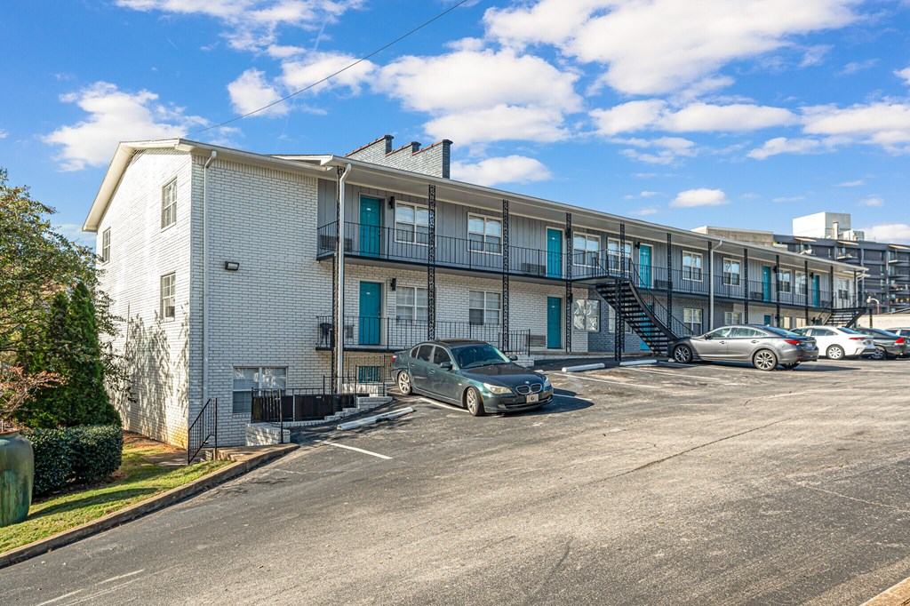 A parking lot in front of a white building with a car parked in the lot.