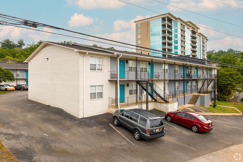 A parking lot with a white building and a red car.
