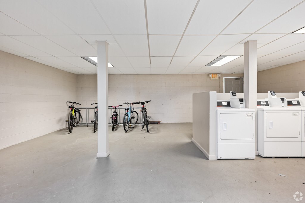 A room with a white ceiling and floor, and a row of bicycles on the left side.