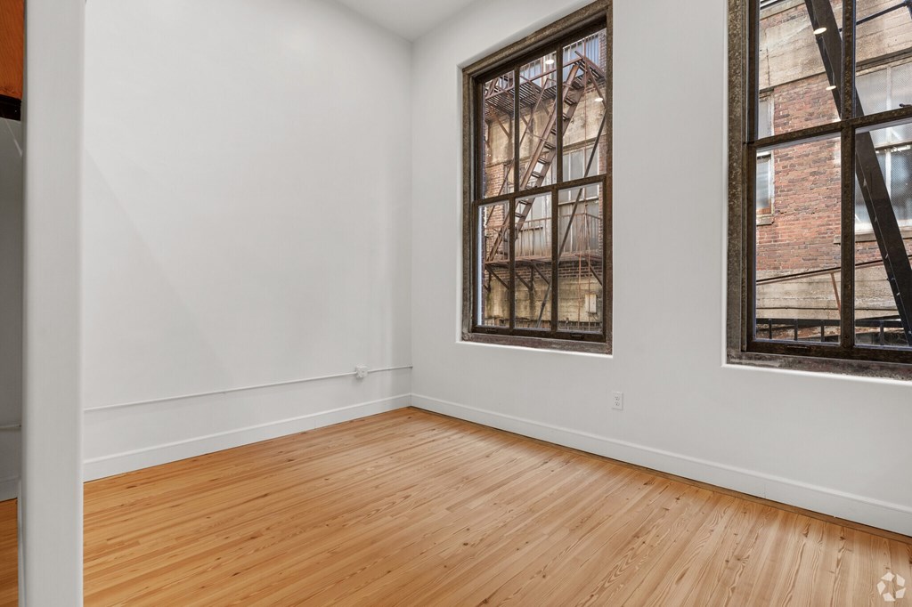 Empty room with wooden floors and a window showing a fire escape.