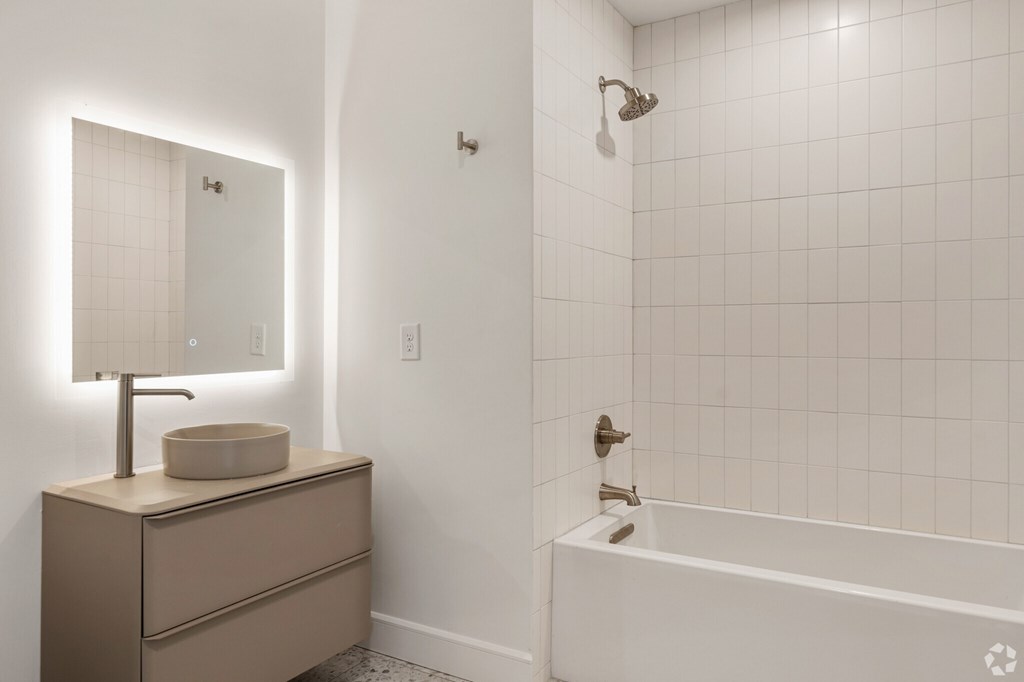 A white tiled bathroom with a sink, mirror, and bathtub.