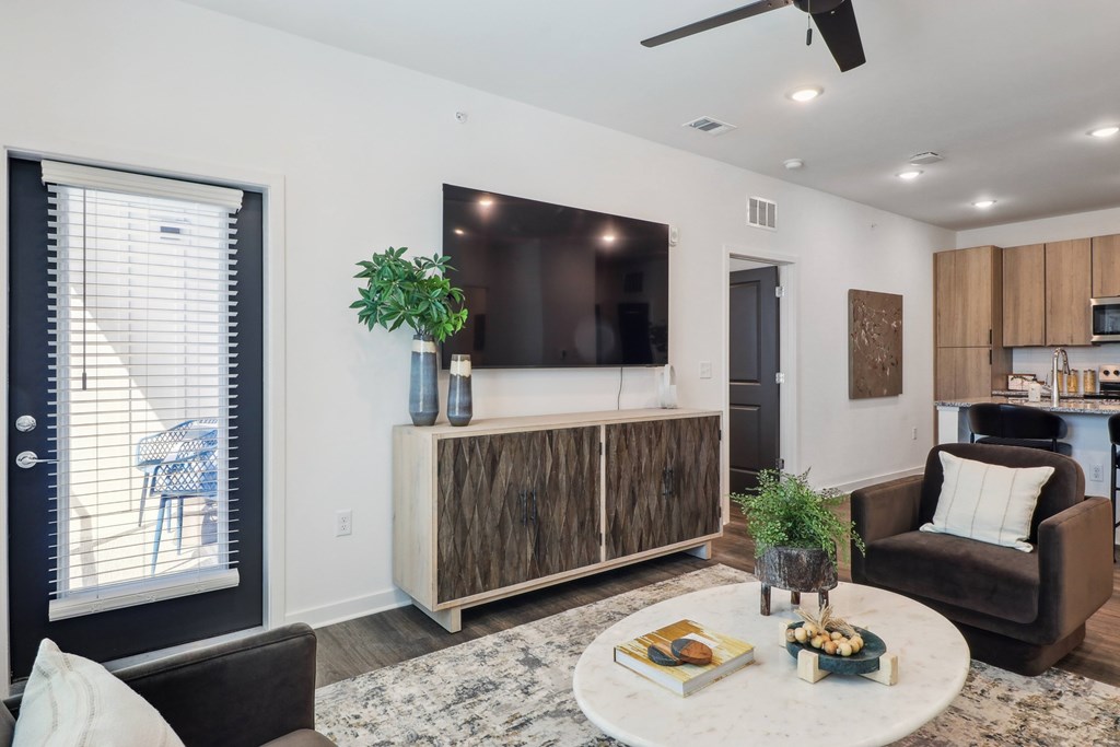 A living room with a black couch, a wooden cabinet, a flat screen TV, and a ceiling fan.