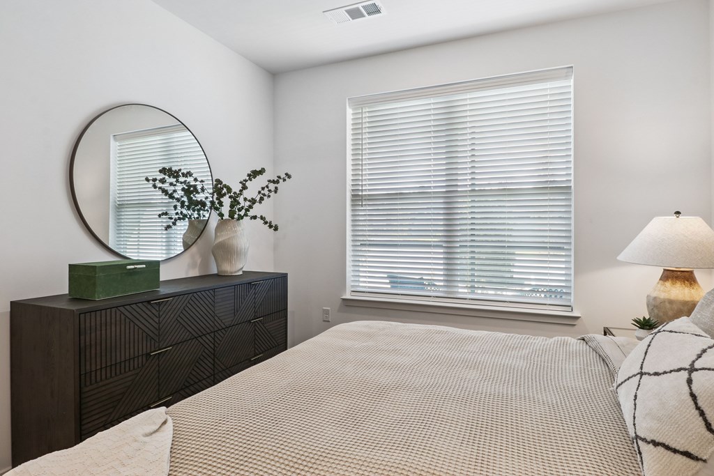 A bedroom with a large bed, a dresser, and a window with blinds.