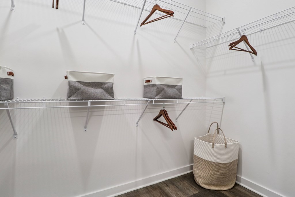 A white closet with clothes hanging and a basket on the floor.