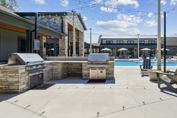 A patio area with a grill, seating, and a pool.