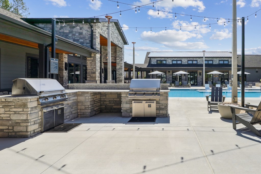 A patio area with a grill, seating, and a pool.