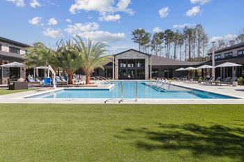 A large swimming pool in the middle of a grassy area with a building in the background.