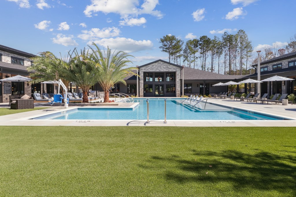 A large swimming pool in the middle of a grassy area with a building in the background.
