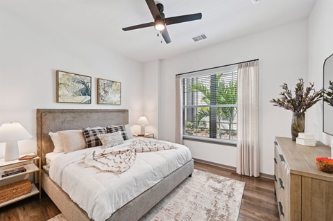 A bedroom with a large bed, a ceiling fan, and a window with a view of trees.