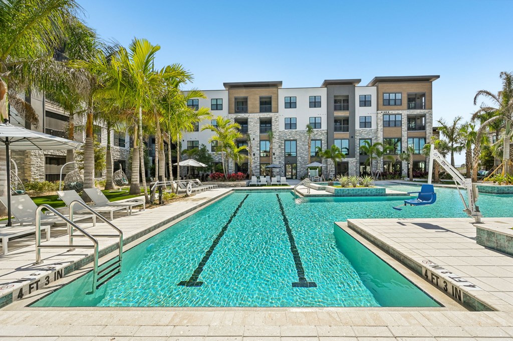 A swimming pool in front of a building with palm trees at The Concord Luxury Apartments, Sarasota, FL